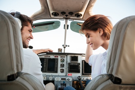 Beautiful young couple looking at each other while sitting inside airplane cabinの写真素材