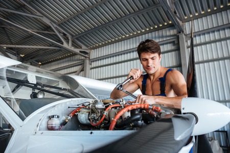 Serious young aircraft mechanic standing and fixing small airplaneの写真素材