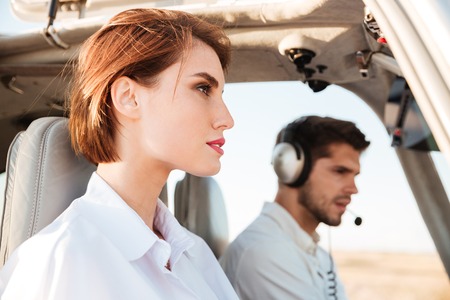 Close up portrait of a young pilot and beautiful stewardess sitting together inside airplane cabin waiting to take offの写真素材