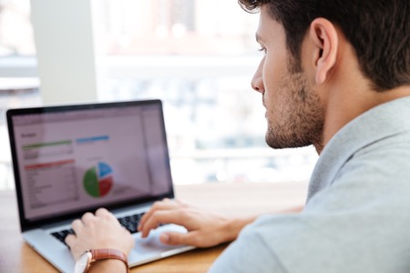 Close up portrait of a young businessman working with laptop and analyzing charts indoorsの写真素材
