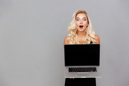 Portrait of a happy excited woman pointing finger on blank laptop computer screen isolated on a white backgroundの写真素材
