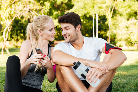 Smiling young woman and personal trainer with smartphone resting after jogging outdoorsの写真素材