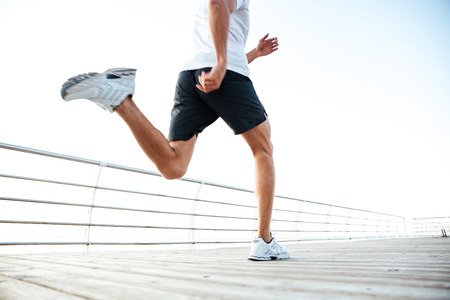 Cropped image of an athlete runner's feet and shoes running along beach pier