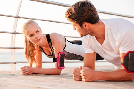 Close up of a young fitness woman and man doing plank exercise together outdoors at the pier
