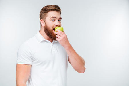 Cheerful young man is eating apple isolated over white backgroundの写真素材