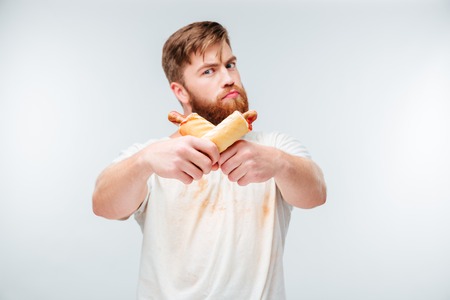 Young bearded man in filthy shirt holding two hotdogs isolated on white backgroundの写真素材