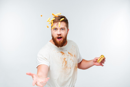 Funny bearded man in dirty shirt throwing french fries isolated on white background