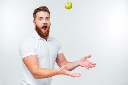 Portrait of handsome funny bearded man throwing apple up isolated on white backgroundの写真素材