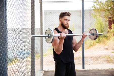 Portrait of a muscular fitness man doing heavy exercise using barbell outdoorsの写真素材