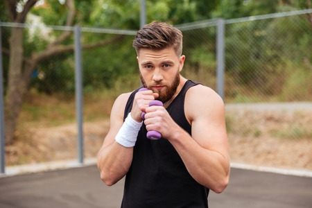 Handsome bearded sports man working out with small dumbbells outdoorsの写真素材