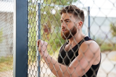 Close up portrait of young bearded man looking through metal urban fence outdoorsの写真素材