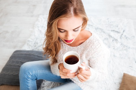 Lovely cute woman with long hair and red lipstick holding tea cup indoorsの写真素材
