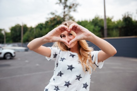 Smiling blonde woman making heart gesture with hands outdoorsの写真素材