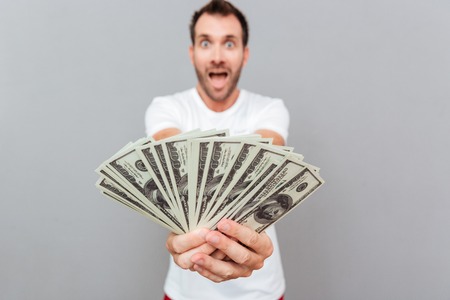 Happy casual man giving money on camera over gray backgroundの写真素材