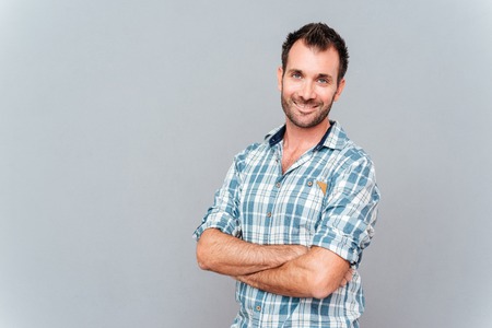 Portrait of a smiling man standing with hands crossed over gray backgroundの写真素材