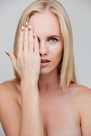 Portrait of a young nude woman covering her eye with palm isolated on a gray backgroundの写真素材