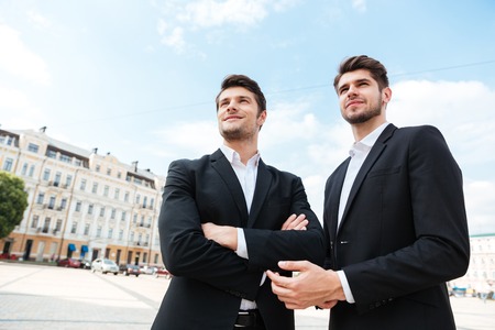 Two happy young businessmen standing outdoors togetherの写真素材