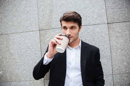 Portrait of attractive young businessman standing and drinking coffeeの写真素材