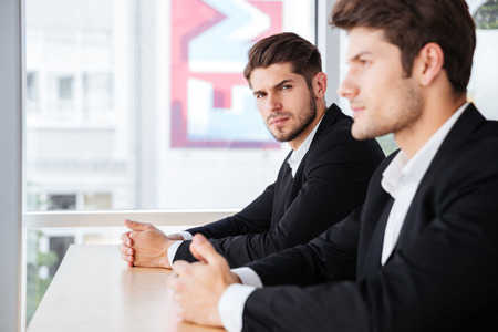 Two handsome young businessmen in black suit sitting in officeの写真素材