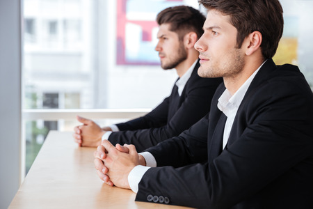 Profile of two confident young businessmen sitting in officeの写真素材