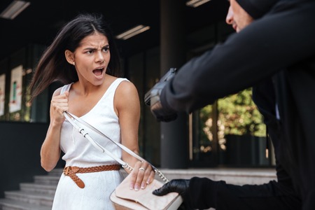 Angry young woman shouting and protecting from man thief with gun on the streetの写真素材