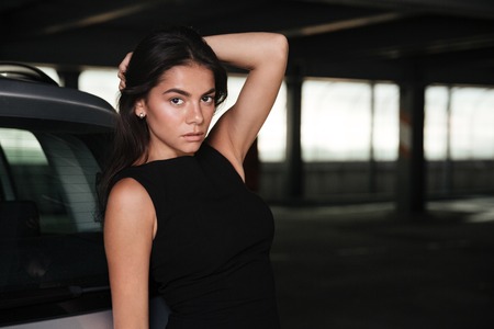 Portrait of gorgeous beautiful young woman in black dress standing on car parkingの写真素材