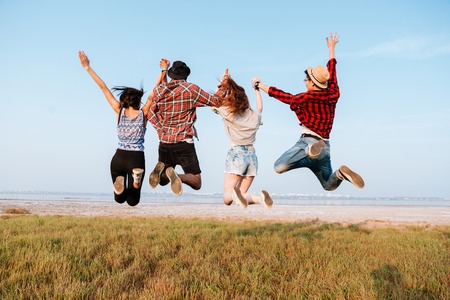 Back view of happy excited young people holding hands and jumping in the air outdoorsの写真素材