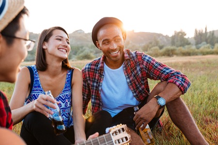 Cheerful multiethnic young couple drinking beer and soda with friends outdoorsの写真素材