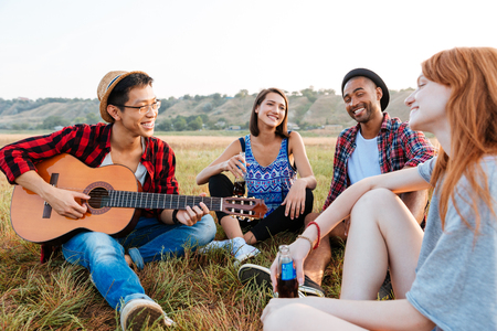 Multiethnic group of smiling young friends playing guitar and singing outdoorsの写真素材