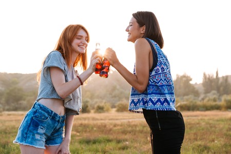 Two cheerful cute young women drinking soda and having fun outdoorsの写真素材