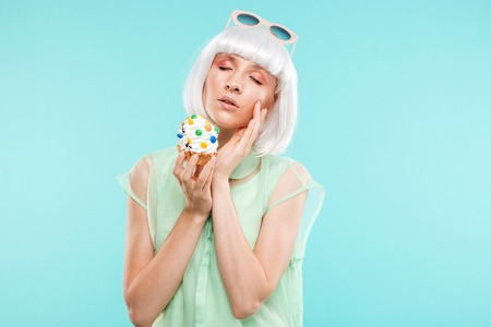 Portrait of attractive sensual blonde young woman with cupcake over blue background
