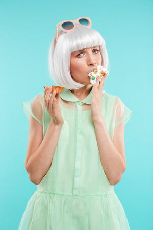 Attrative young woman standing and eating cupcake by handsの写真素材