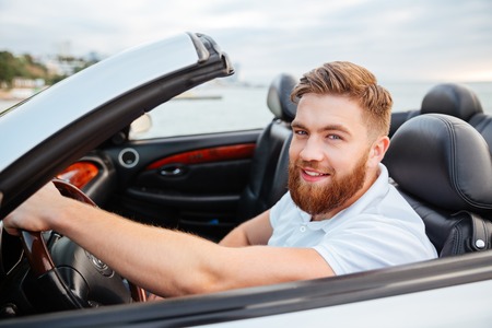 Portrait of young handsome smiling man sitting in his own car