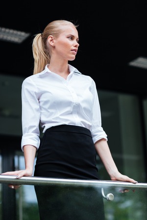 Beautiful blonde businesswoman leaning on the glass railing outdoorsの写真素材