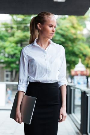 Close up portrait of a smart business woman with laptop standing at the glass balcony outdoorsの写真素材