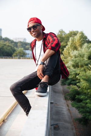 Photo of cheerful dark skinned man wearing sunglasses. Sitting against nature background.の写真素材