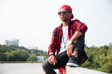 Picture of attractive dark skinned man wearing sunglasses. Sitting against nature background.の写真素材