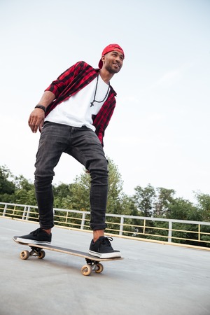 Picture of young dark skinned man wearing sunglasses and cap skateboarding. Against the nature background.の写真素材