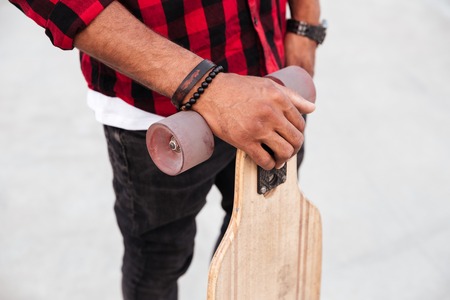 Picture of young dark skinned guy holding his skateboard. Against the nature background.の写真素材