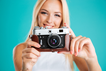 Close up portrait of a young attractive woman with retro camera isolated on the blue backgroundの写真素材