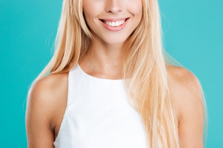 Cropped image of a smiling blonde woman in white top isolated on the blue backgroundの写真素材