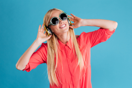 Portrait of a happy pretty young woman listening music with headphones over blue backgroundの写真素材