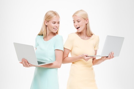 Picture of two happy young women looking at their laptops. Isolated over white background.の写真素材
