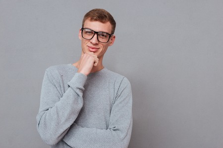 Young man in glasses. hand near the face. looking at camera. isolated gray background