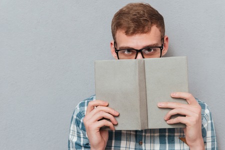 Student in glasses with book in studio. looking at camera. isolated gray backgroundの写真素材