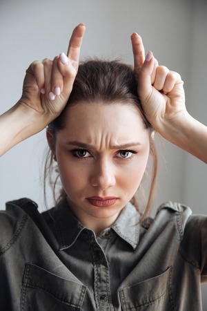 Serious woman in shirt in studio. looking at camera. showing horns. isolated gray backgroundの写真素材