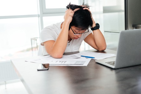 Asian man in panic by the table with documents and laptop