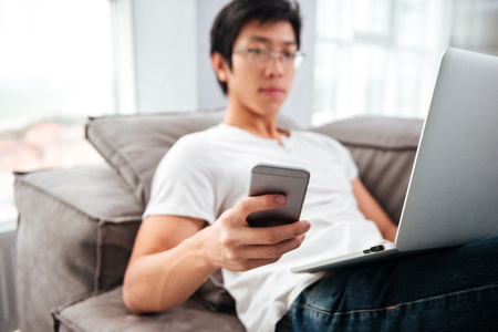 Asian man with laptop and phone on sofa. side viewの写真素材