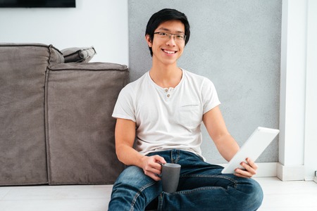 Asian man sitting with coffee and tablet near the windowの写真素材