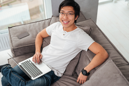 Above portrait of asian man with laptop on sofa. looking at cameraの写真素材